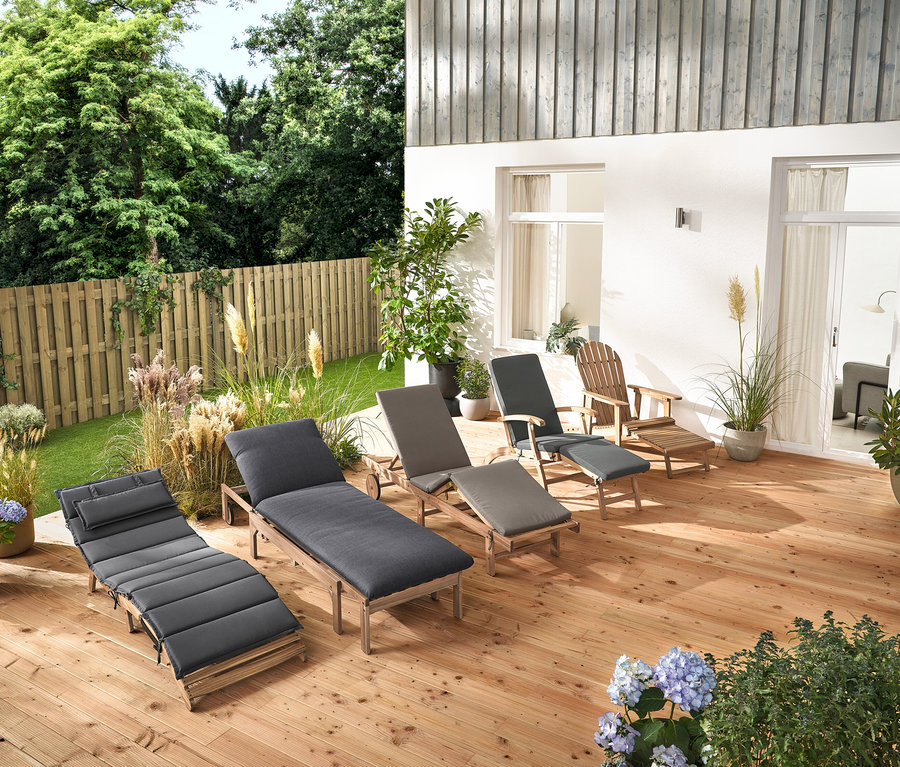 Na dřevěné terase stojí několik zahradních lehátek a zahradní křeslo Adirondack s výsuvnou podnožkou z dřeva.