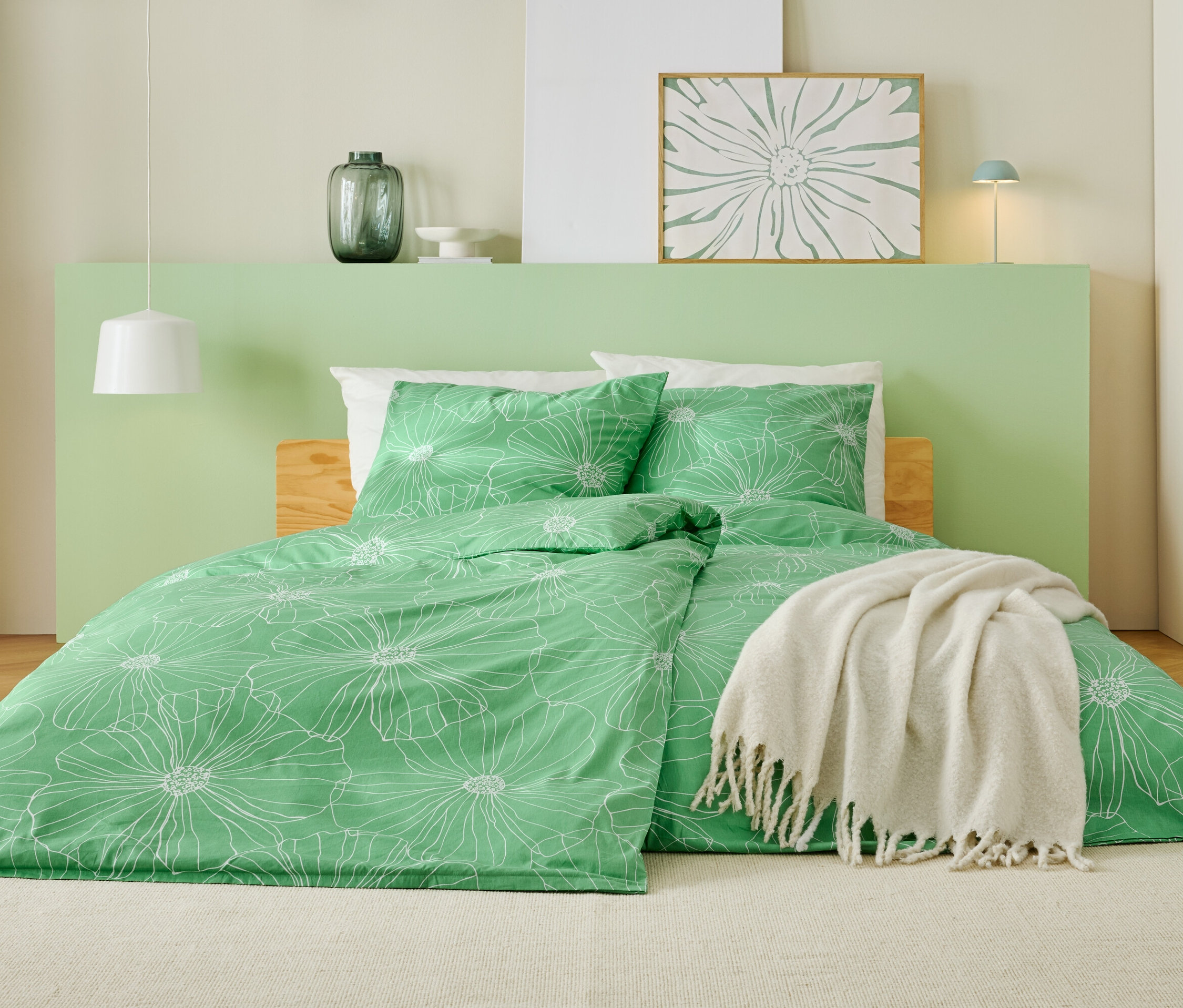 Postel se zeleným povlečením s bílým květinovým vzorem, bílou dekou a světle zeleným čelem.
