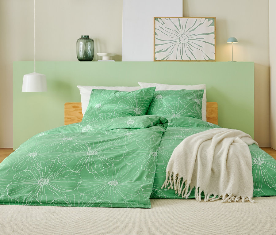 Postel se zeleným povlečením s bílým květinovým vzorem, bílou dekou a světle zeleným čelem.