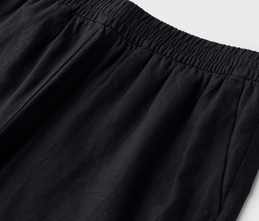 Detailní záběr na pas černých kalhot s elastickým pasem.