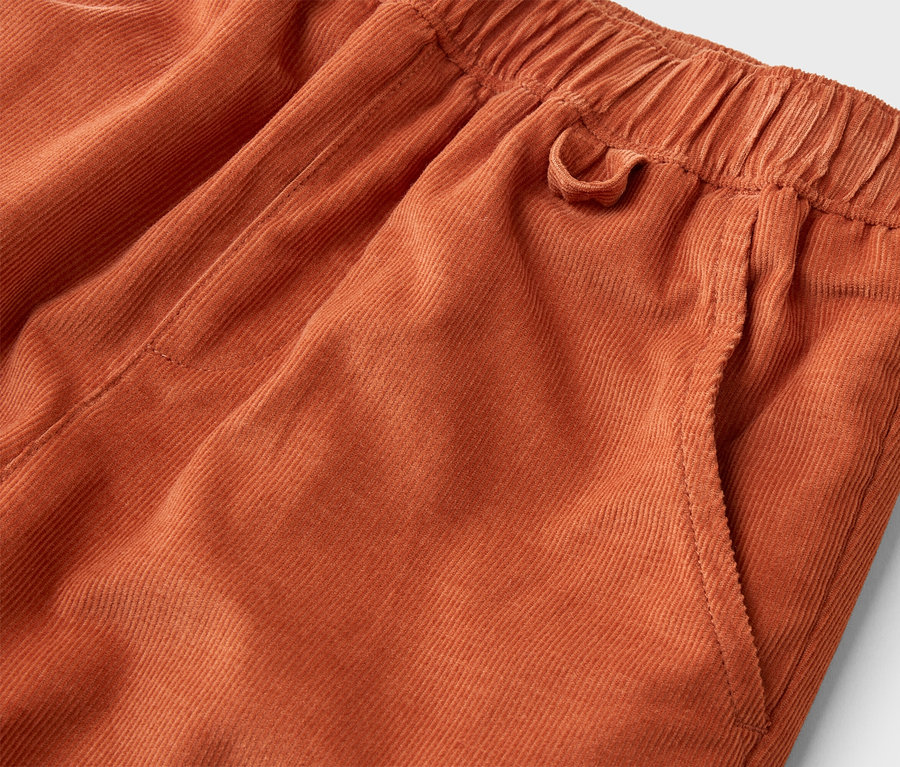Detail oranžových manšestrových kalhot s elastickým pasem a boční kapsou.