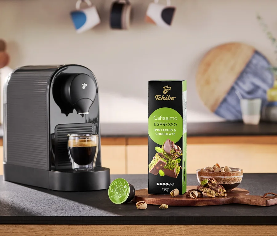 Kávovar nalévá kávu do šálku vedle balení kapslí Cafissimo Flavoured Espresso.