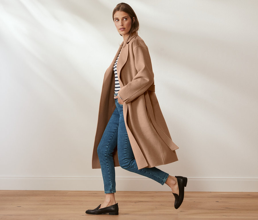 Žena kráčí a má na sobě vlněný kabát s kašmírem, džíny a mokasíny.