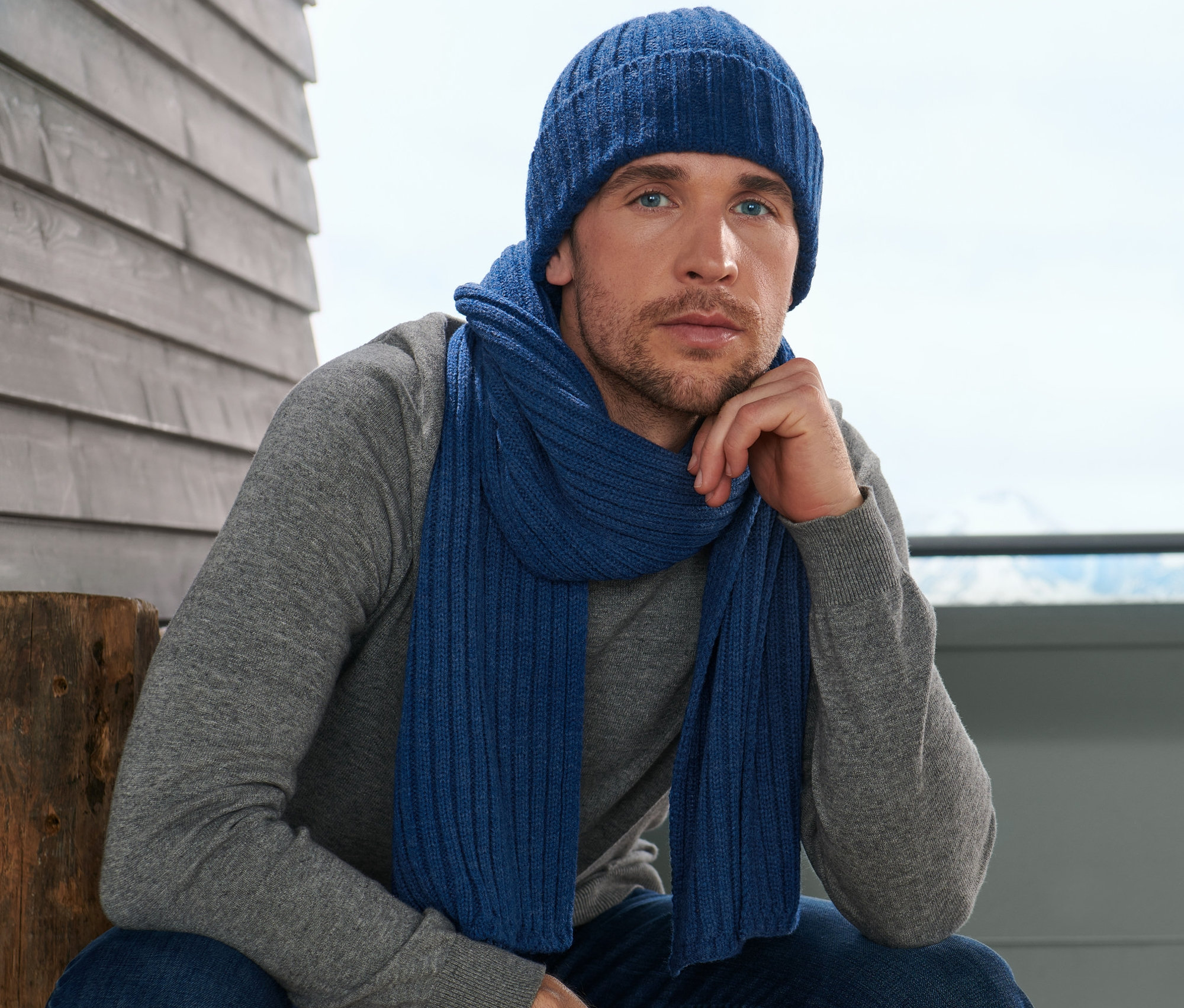 Muž sedí a má na sobě pletenou šálu a čepici.