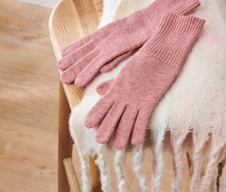 Pletené rukavice s vlnou, růžové, leží na dřevěné židli s bílou šálou.