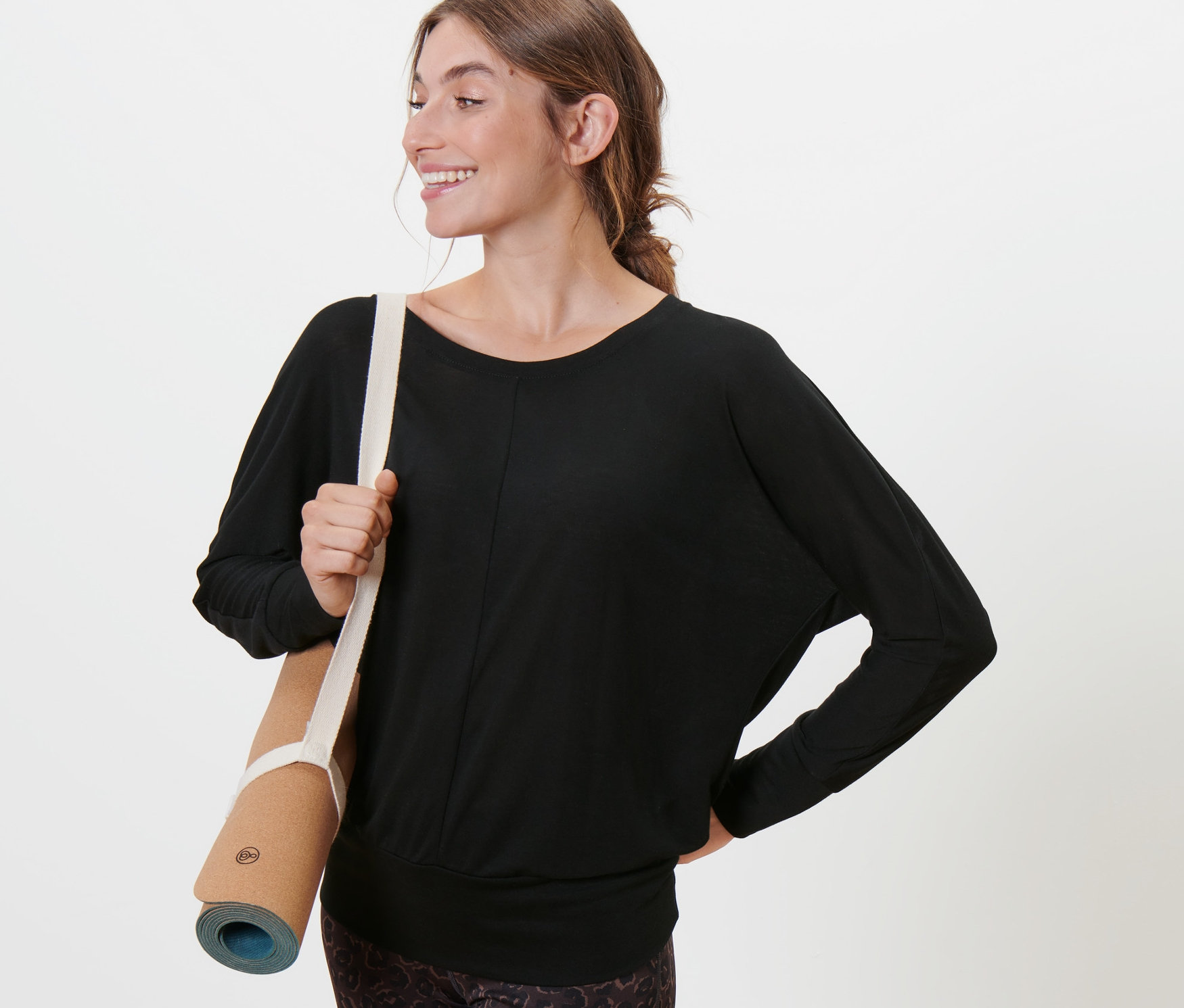 Žena drží podložku na jógu a má na sobě černé sportovní triko na jógu.