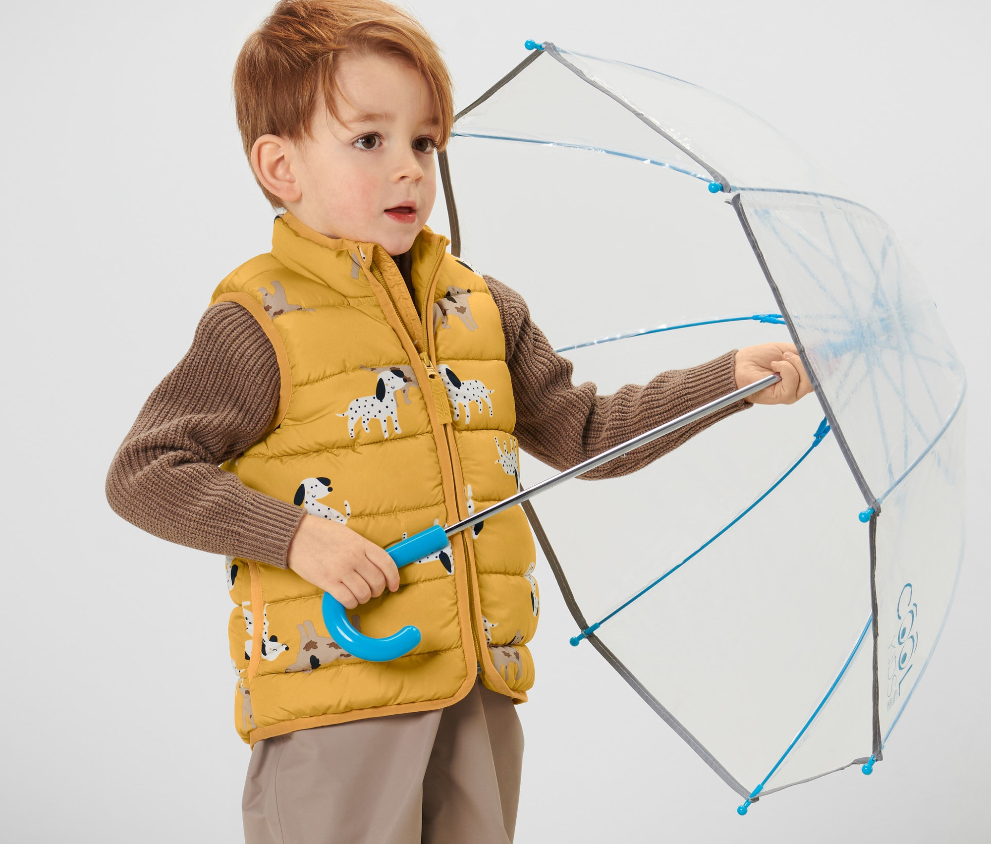 Chlapec drží otevřený deštník a má na sobě dětskou prošívanou vestu.