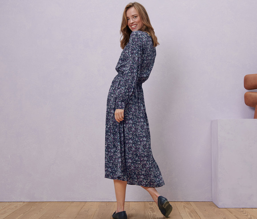 Žena se usmívá přes rameno a pózuje v květovaných midi šatech.