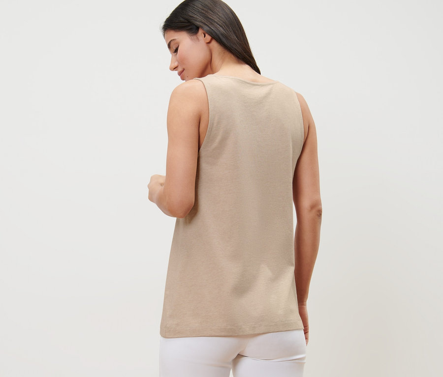 Žena zády ke kameře má na sobě béžový melírovaný top s knoflíkovou légou a bílé kalhoty.