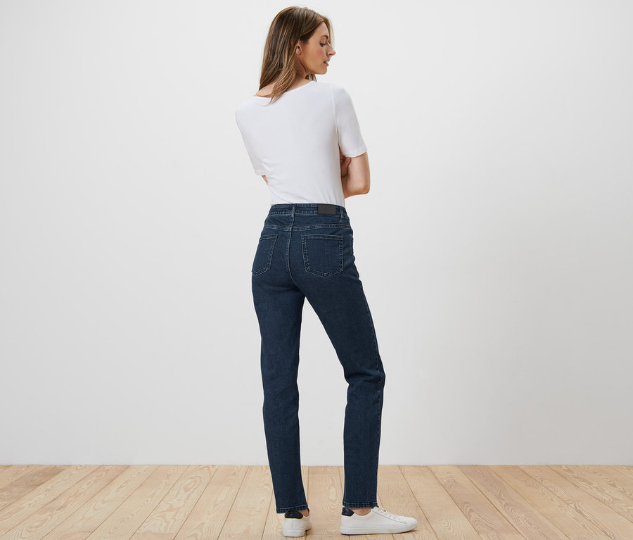 Žena pózuje zády ke kameře a má na sobě rovné džíny »Kira«, bílé tričko a tenisky.