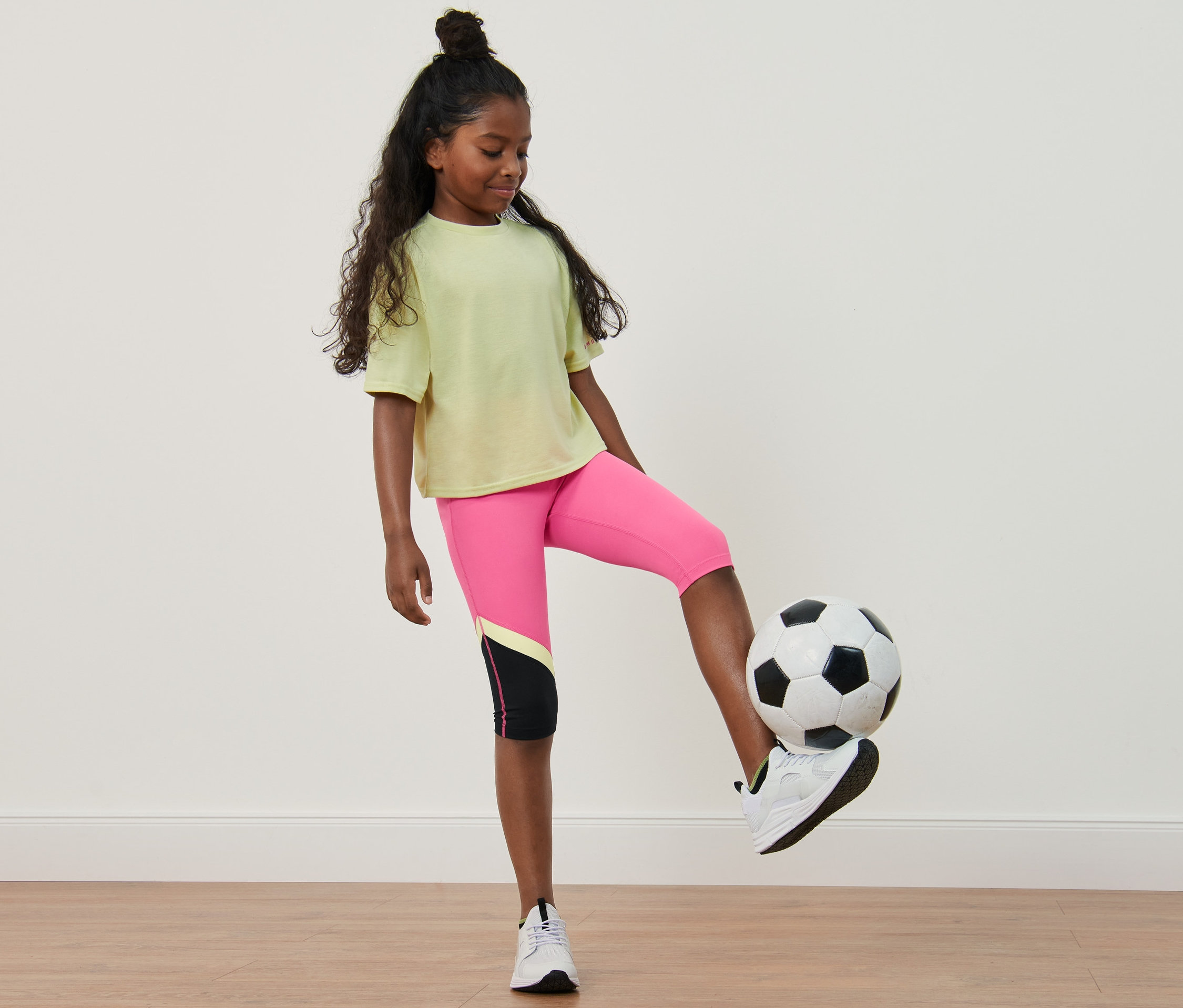 Dívka si hraje s fotbalovým míčem, má na sobě dětské sportovní legíny (2 ks).
