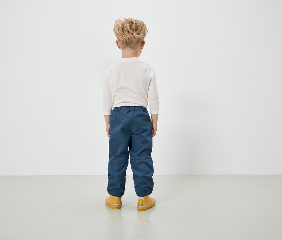 Chlapec v modrých kalhotách a žlutých botách stojí zády ke kameře.