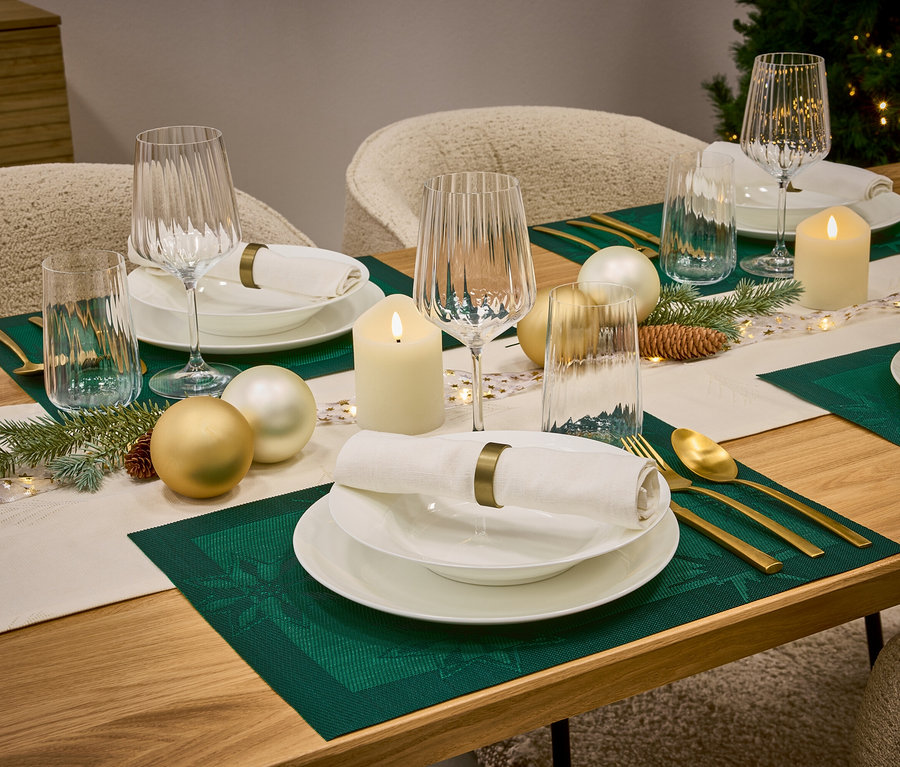 Prostřený stůl s bílým nádobím, sklenicemi, zlatými příbory, zelenými prostírkami a vánočními ozdobami.