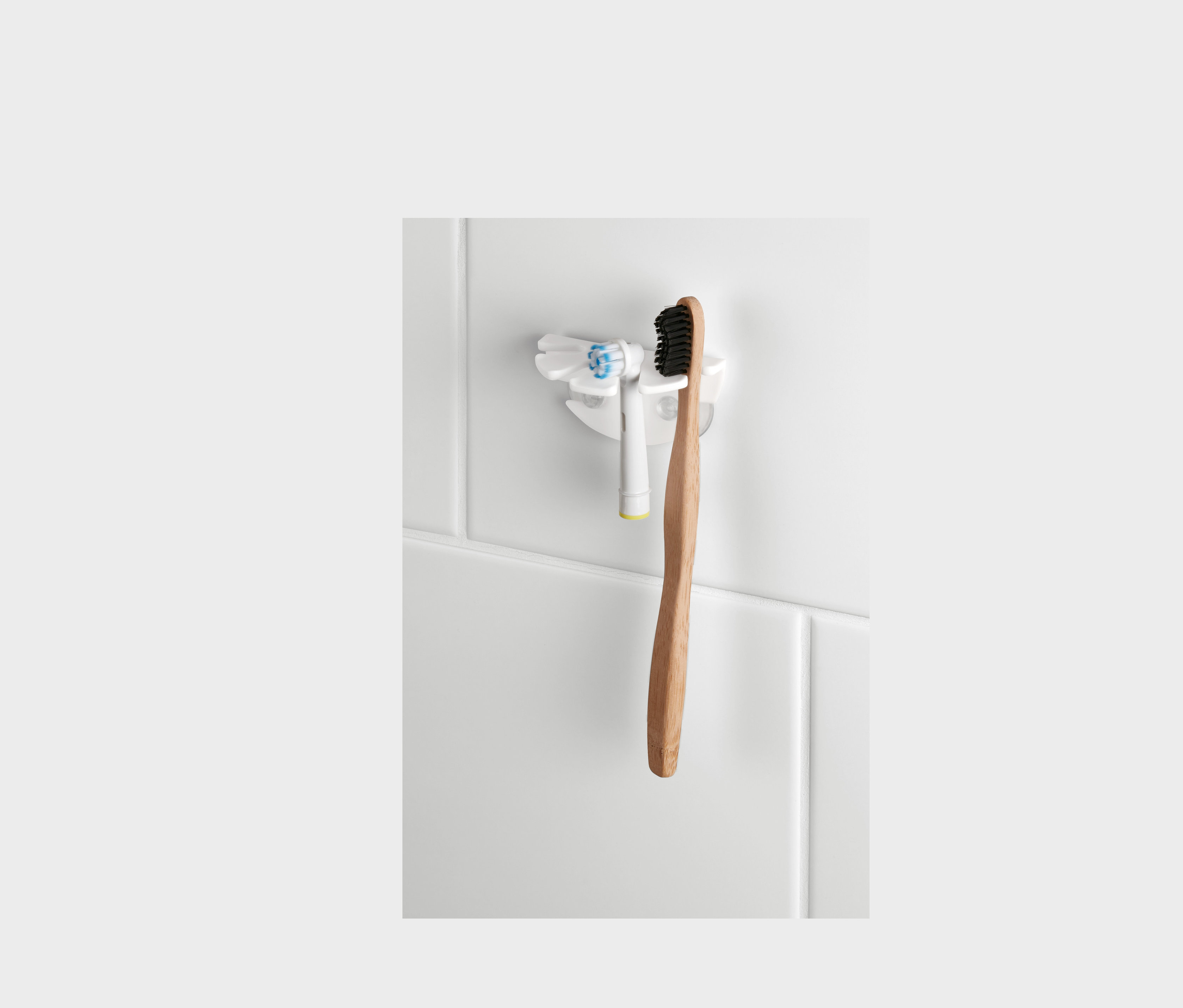 Držák na zubní kartáčky s přísavkou drží elektrický kartáček a dřevěný kartáček na bílých kachličkách.