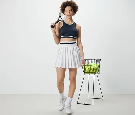 Žena drží tenisovou raketu a má na sobě modrou sportovní podprsenku »Crop Top«.