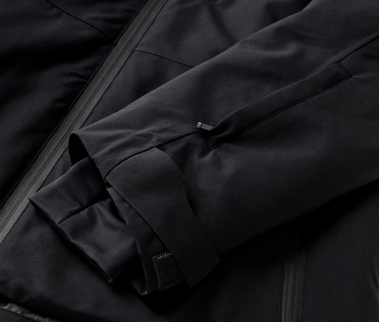 Detail černé bundy s rukávem a kapsou na zip.