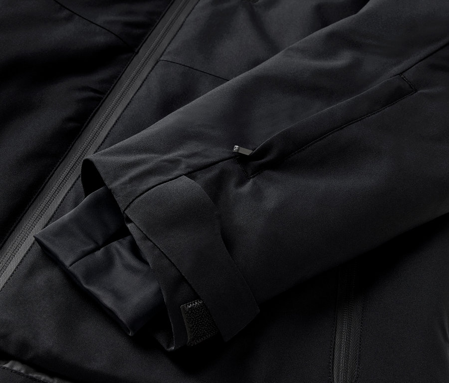 Detail černé bundy s rukávem a kapsou na zip.