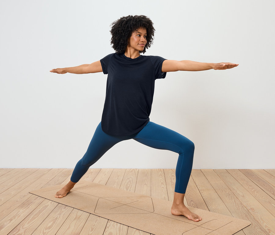 Žena v modrých legínách a černém tričku cvičí jógu na podložce.