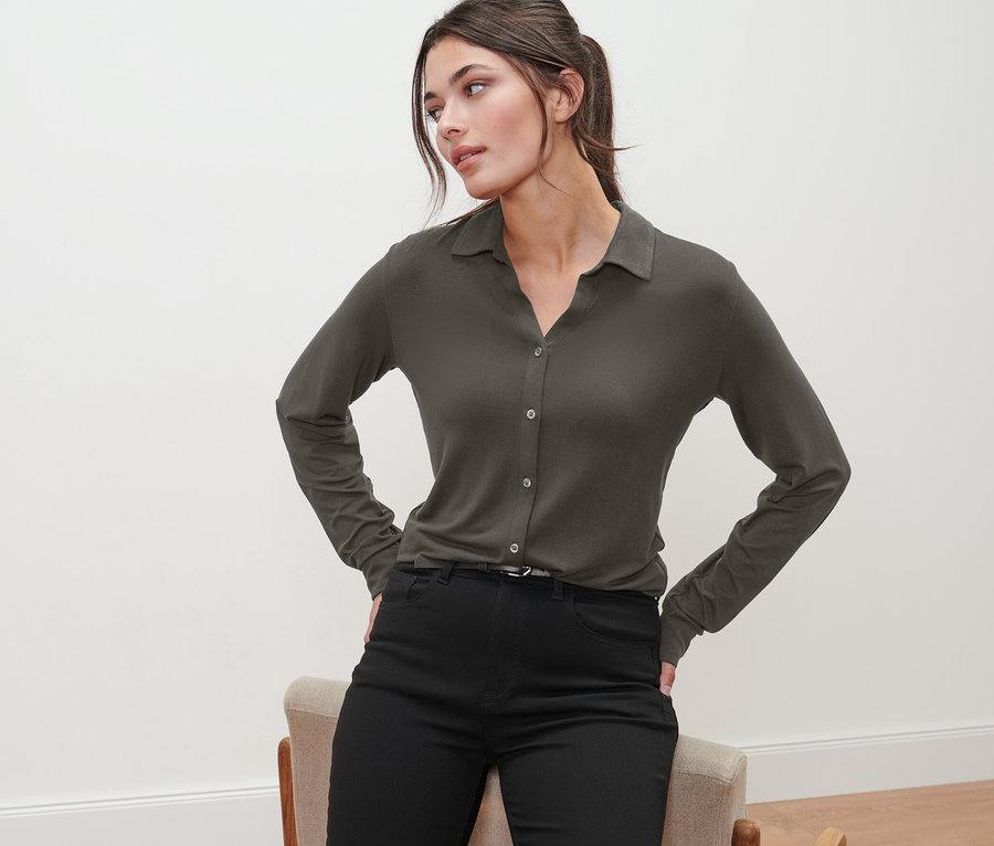 Žena pózuje v olivově zeleném halénkovém triku s knoflíkovou légou a černých kalhotách.
