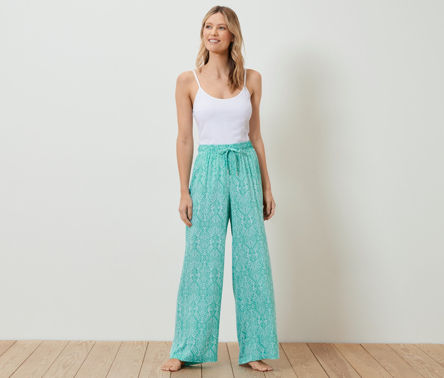 Žena stojí a má na sobě bílý top a pohodlné kalhoty.