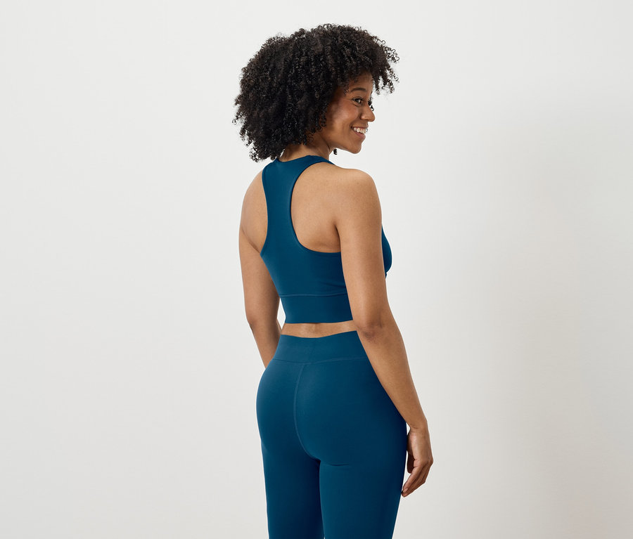 Žena se dívá přes rameno, oblečená v modré sportovní soupravě.