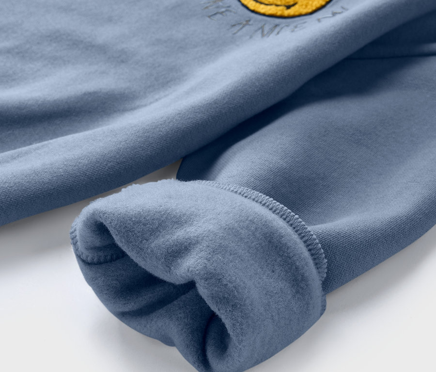 Detail modré dětské mikiny SMILEYWORLD® s vnitřní stranou s chloumky a žlutým smajlíkem.