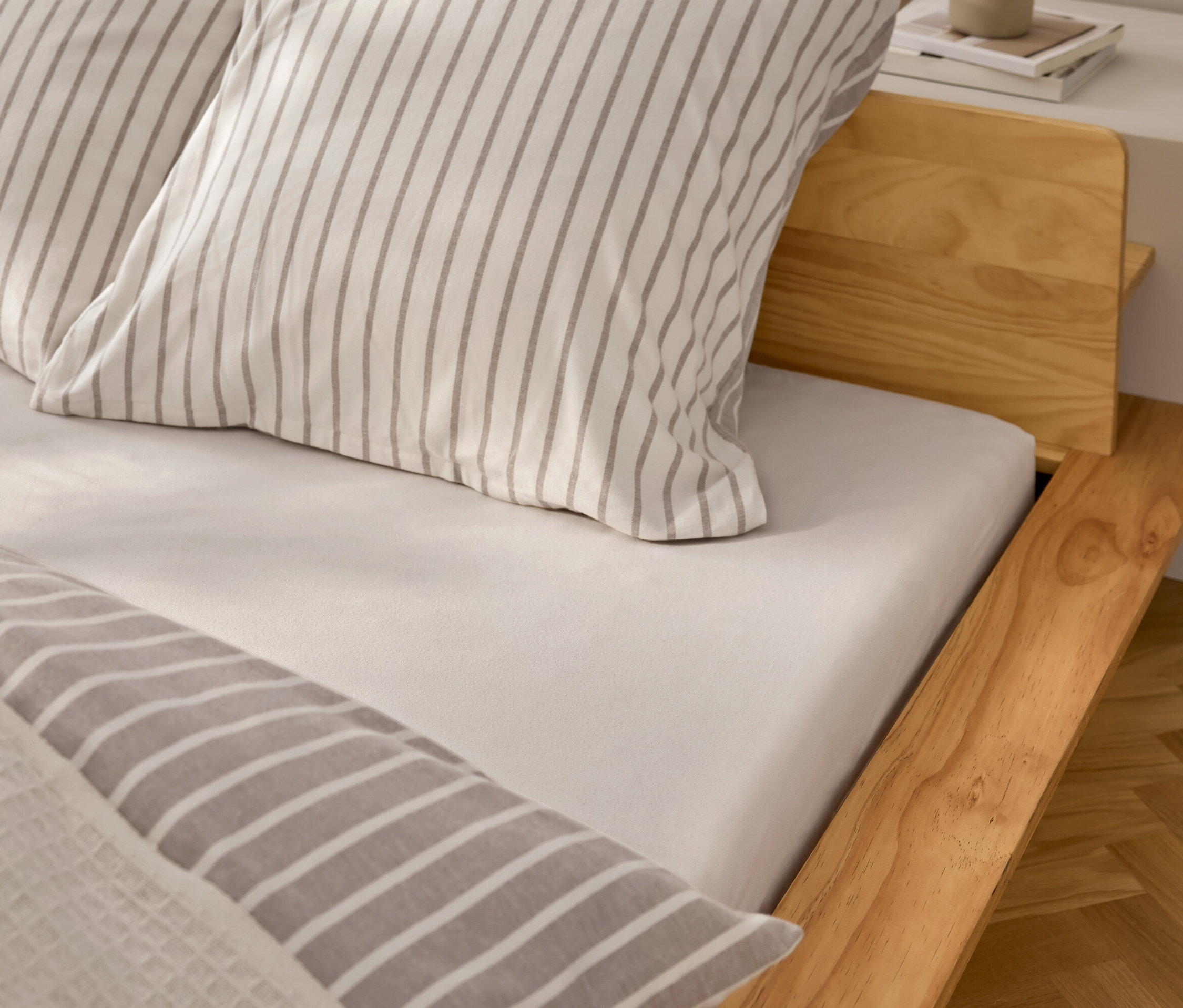 Detail pohledu na postel s bílým prostěradlem a polštáři s šedými pruhy.