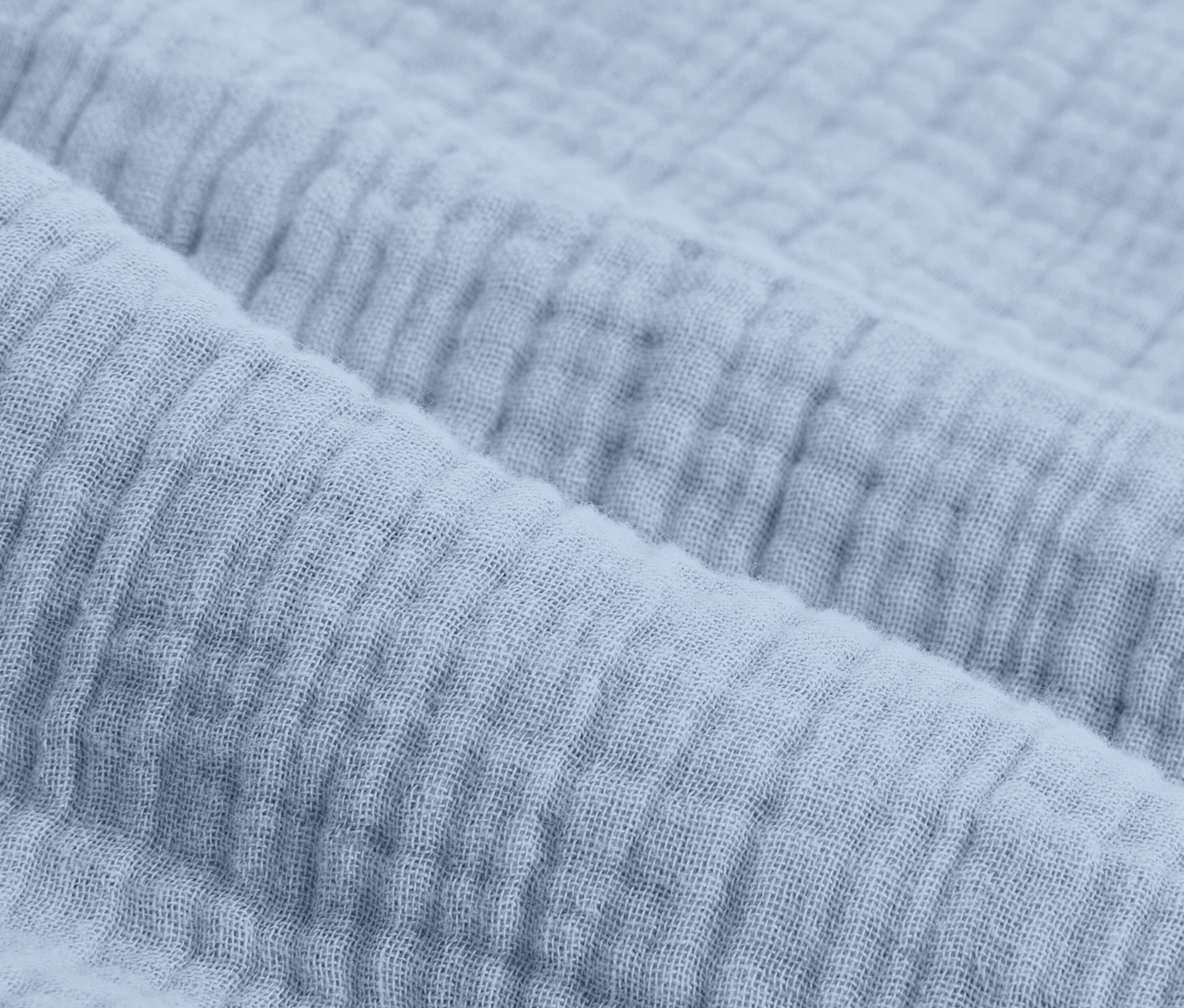 Detailní záběr světle modrého mušelínového povlečení standardní velikosti.