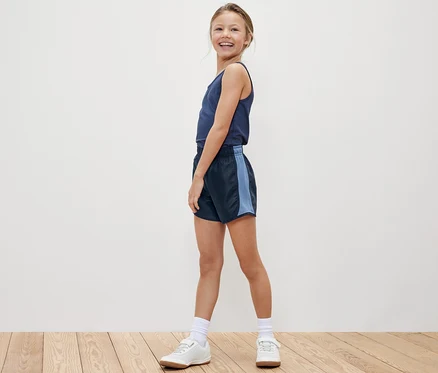 Usmívající se dívka pózuje v tílku a sportovních šortkách Dětské sportovní šortky, 2 ks.