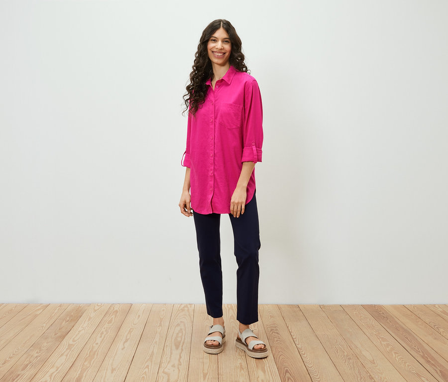 Žena stojí a má na sobě dlouhou lněnou halenku růžové barvy.