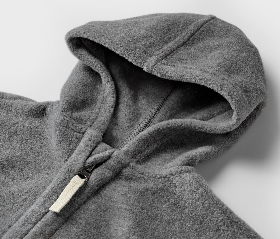 Detail šedé fleecové bundy pro miminka s kapucí a zipem.