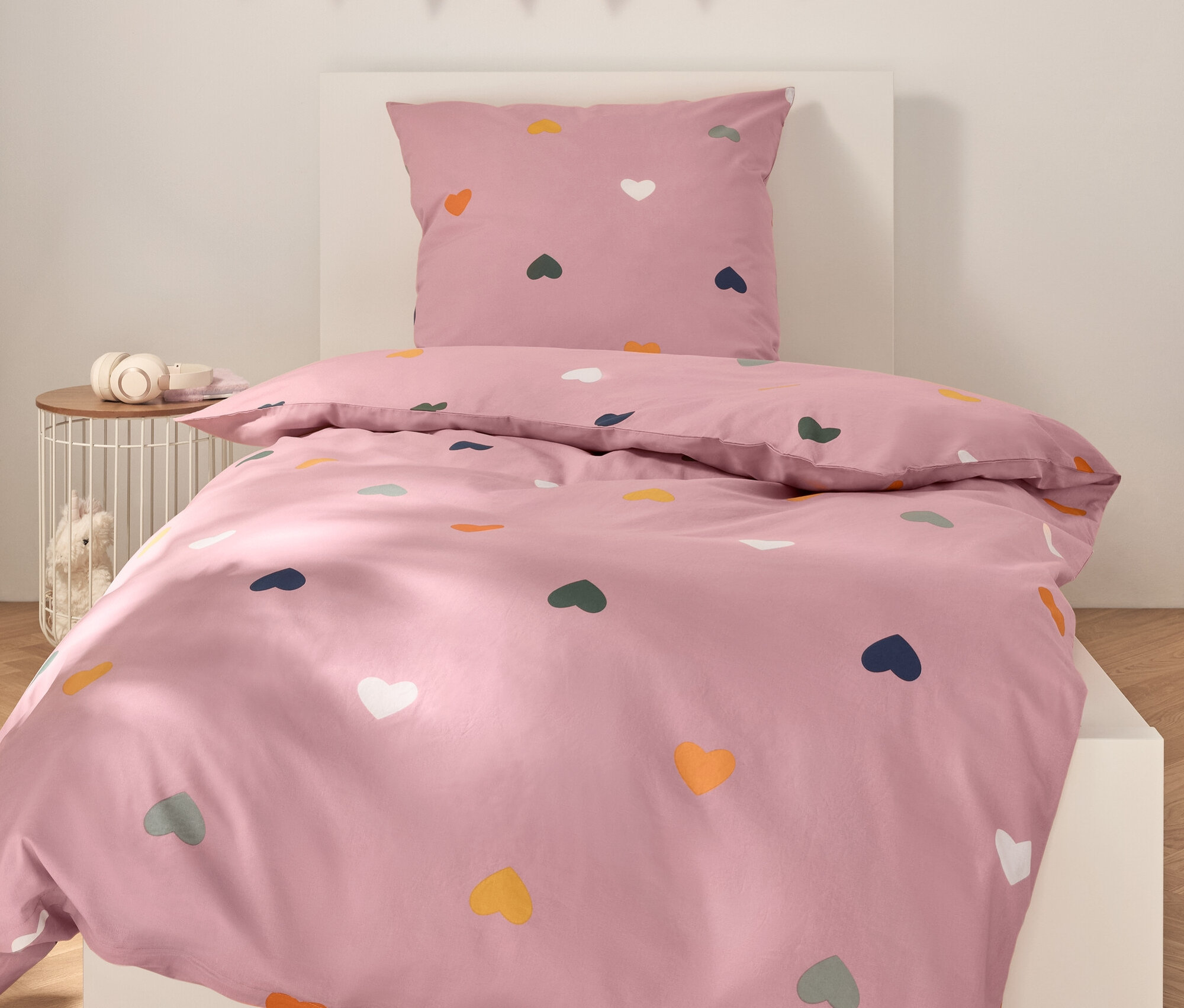 Růžové povlečení s barevnými srdíčky na bílé posteli.