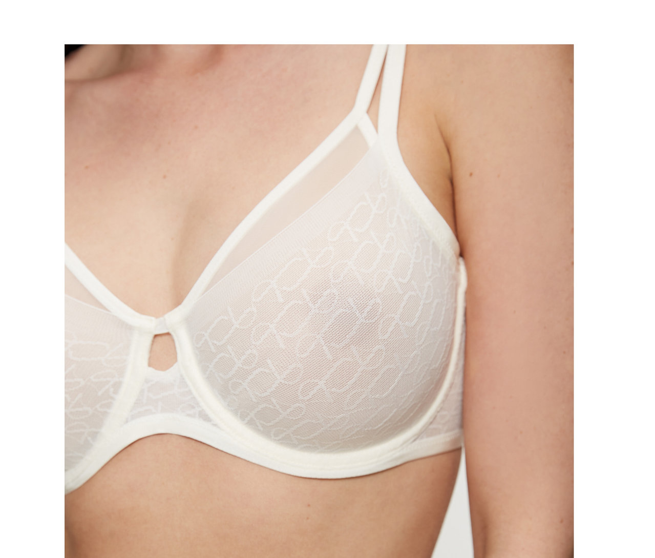 Žena má na sobě zmenšující podprsenku Triumph Signature Sheer v barvě ecru white, se vzorovanými průsvitnými košíčky a malým výřezem uprostřed.