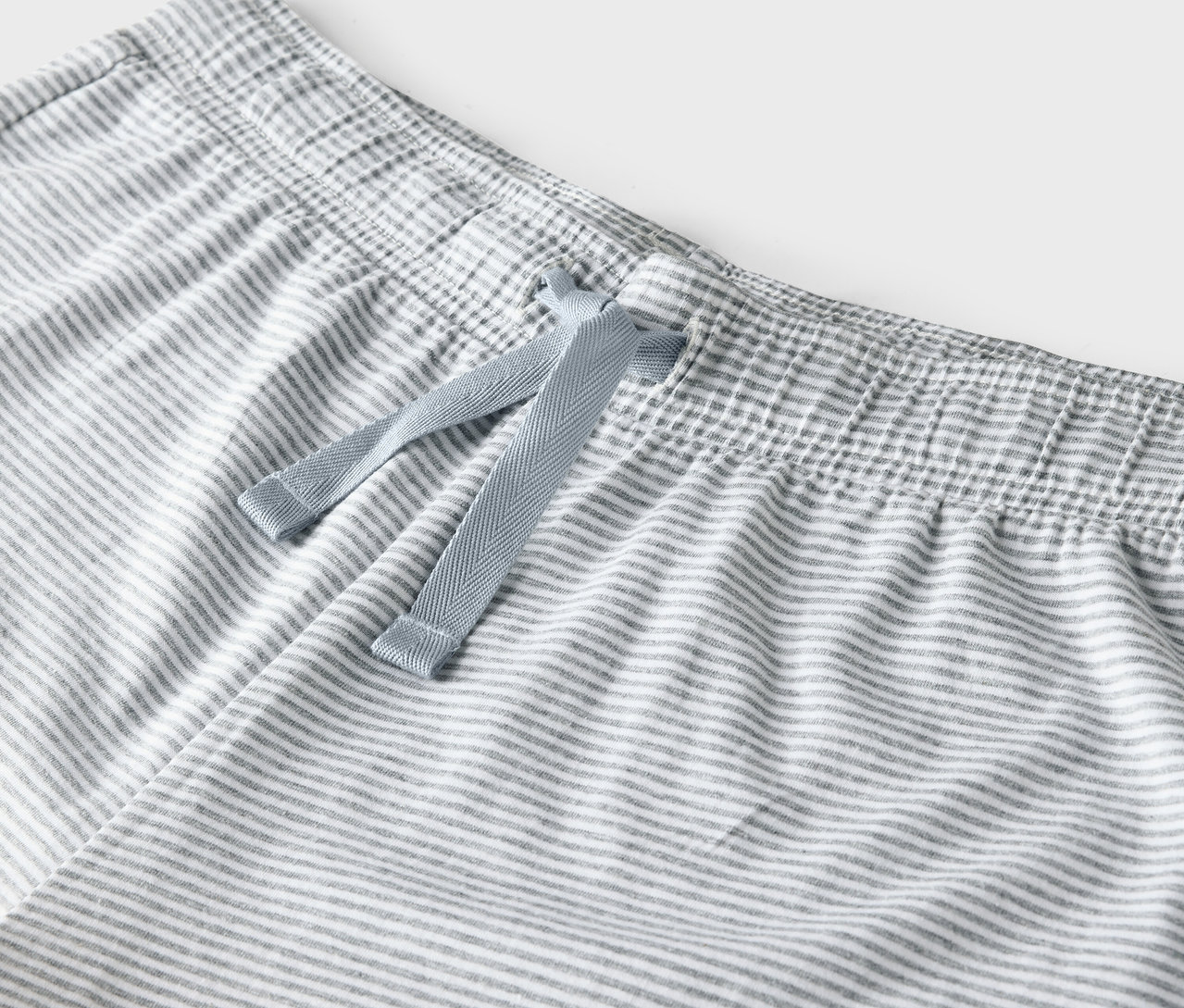 Detail šedobílých pruhovaných kalhot s modrou stahovací šňůrkou v pase.