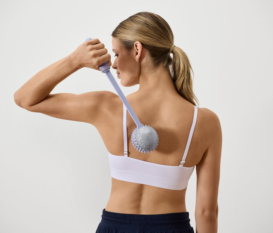 Zezadu pohled na ženu, která si masíruje záda masážním přístrojem s dlouhou rukojetí.