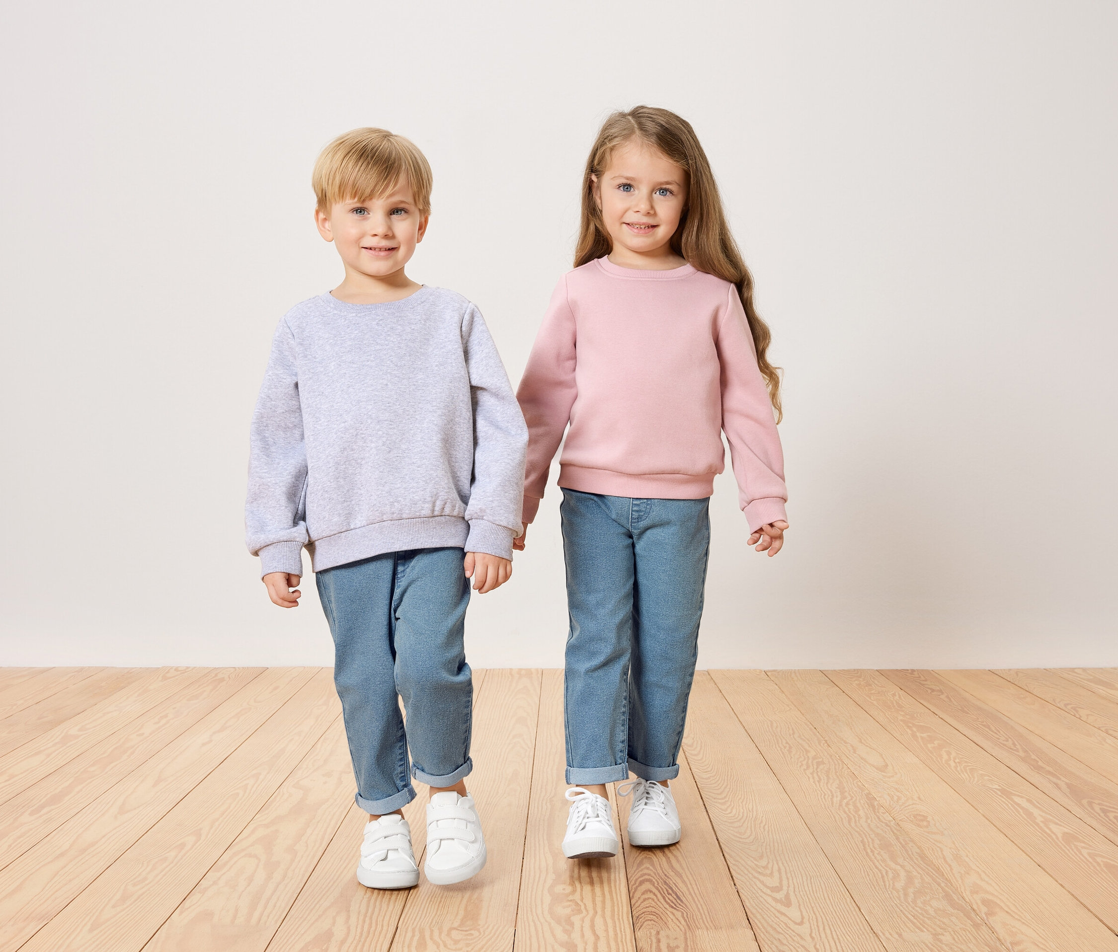 Chlapec v šedé mikině a dívka v růžové mikině se drží za ruce.