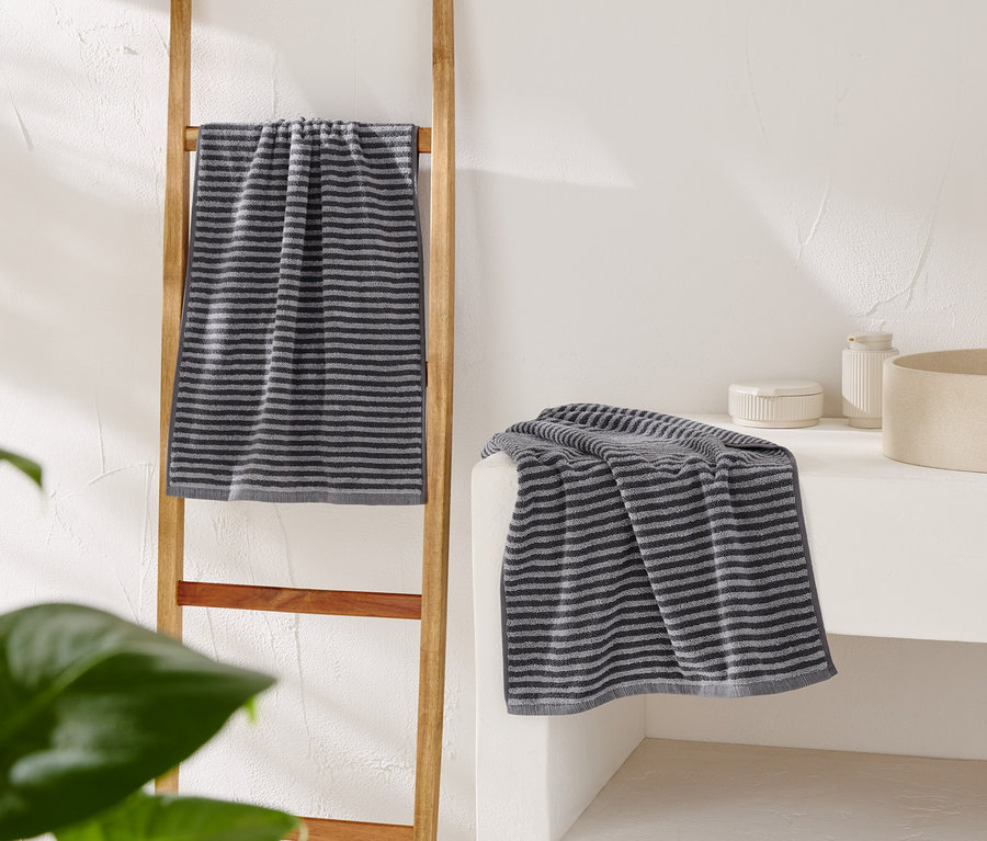 Pruhovaný šedý ručník visí na dřevěném žebříku a další leží na bílém umyvadle vedle béžového umyvadla.