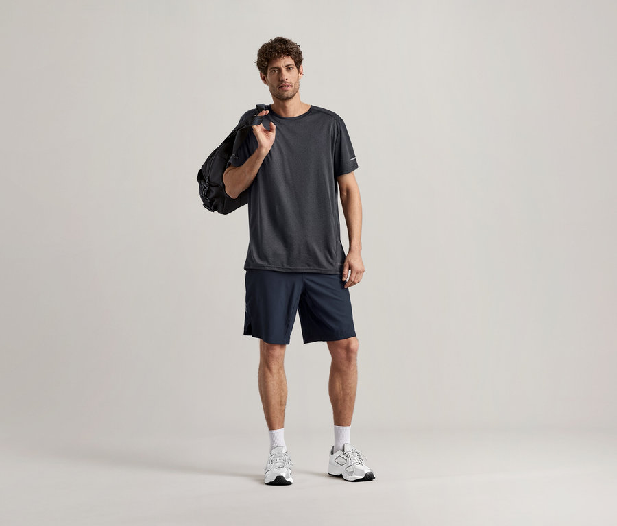 Muž v antracitovém sportovním tričku a sportovní taškou přes rameno.