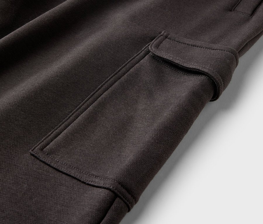 Detail hnědých cargo kalhot s našitou kapsou a zapínáním na knoflík na bílém pozadí.