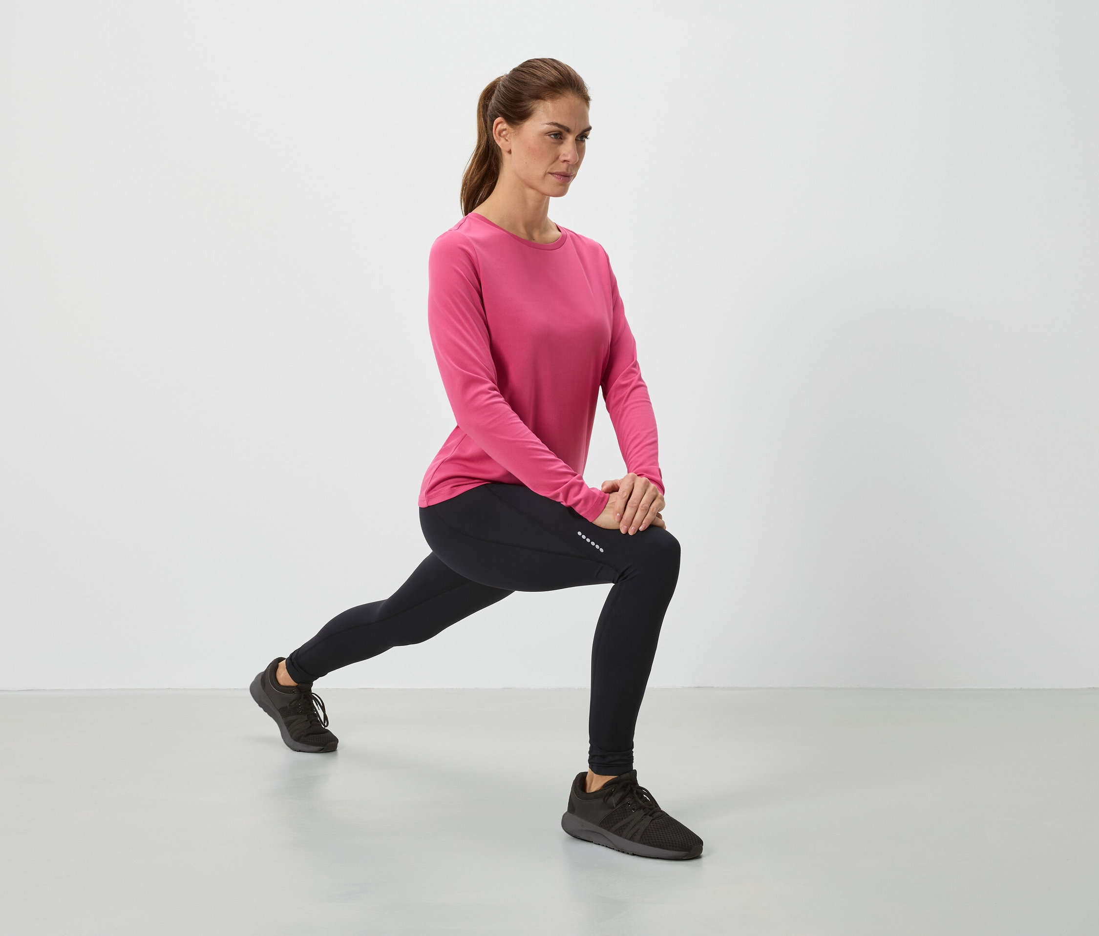 Žena v růžovém topu a černých legínách se protahuje.