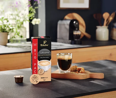 Na lince stojí balení kapslí Cafissimo Decaffeinato, vedle je šálek kávy a kapsle.