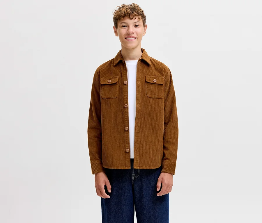 Usmívající se mladý muž v hnědé manšestrové košili Jack & Jones Regent, bílém tričku a modrých džínách.