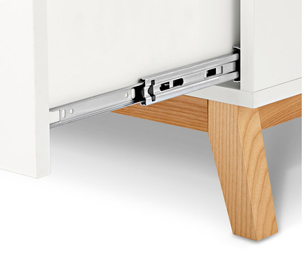 Detail bílé komody s otevřenou zásuvkou a dřevěnýma nohama.