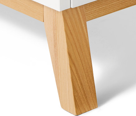 Detail bílé komody s nohami ze světlého dřeva.