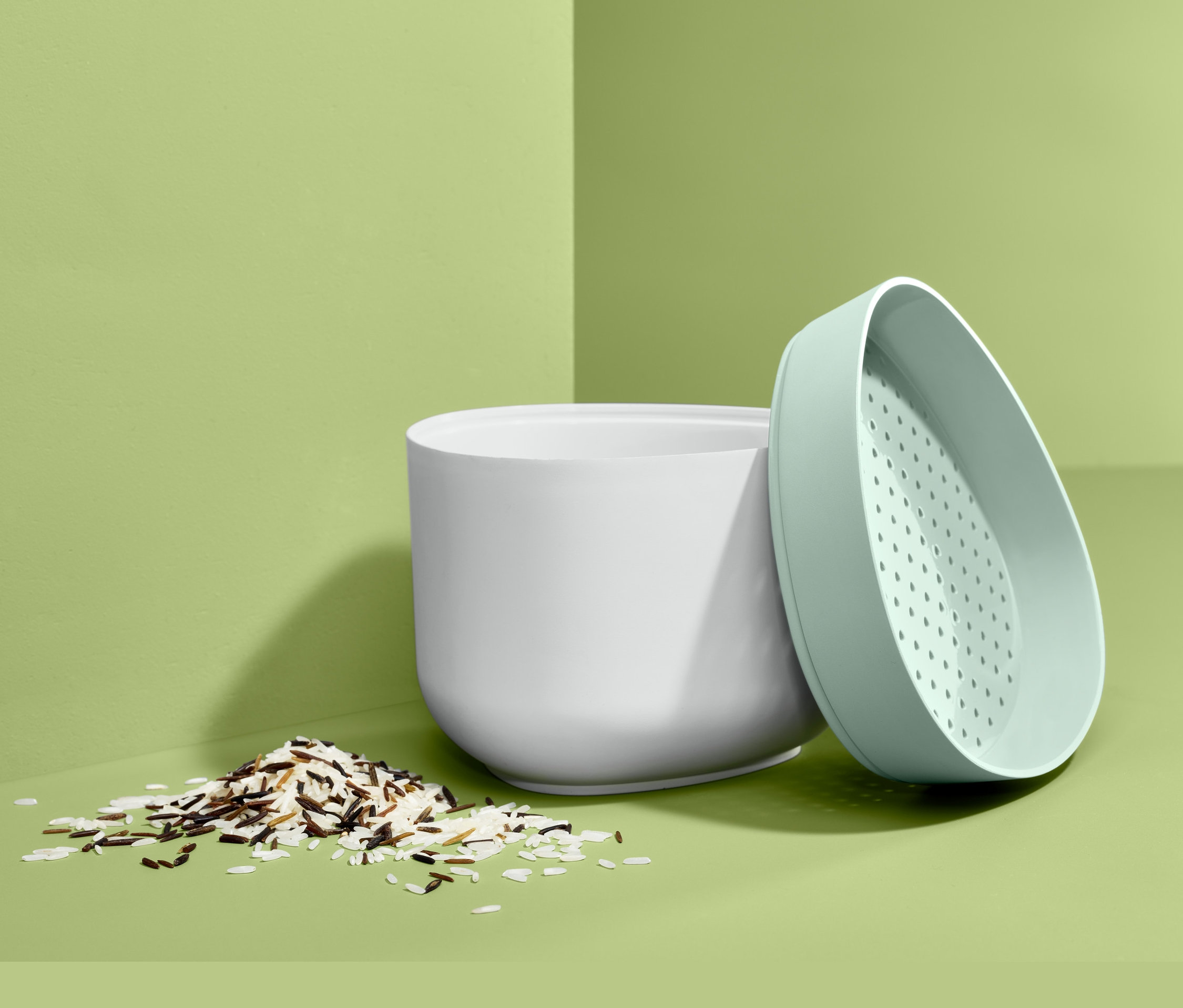 Bílá nádoba na vaření rýže v mikrovlnné troubě s hromádkou rýže a zeleným víkem.