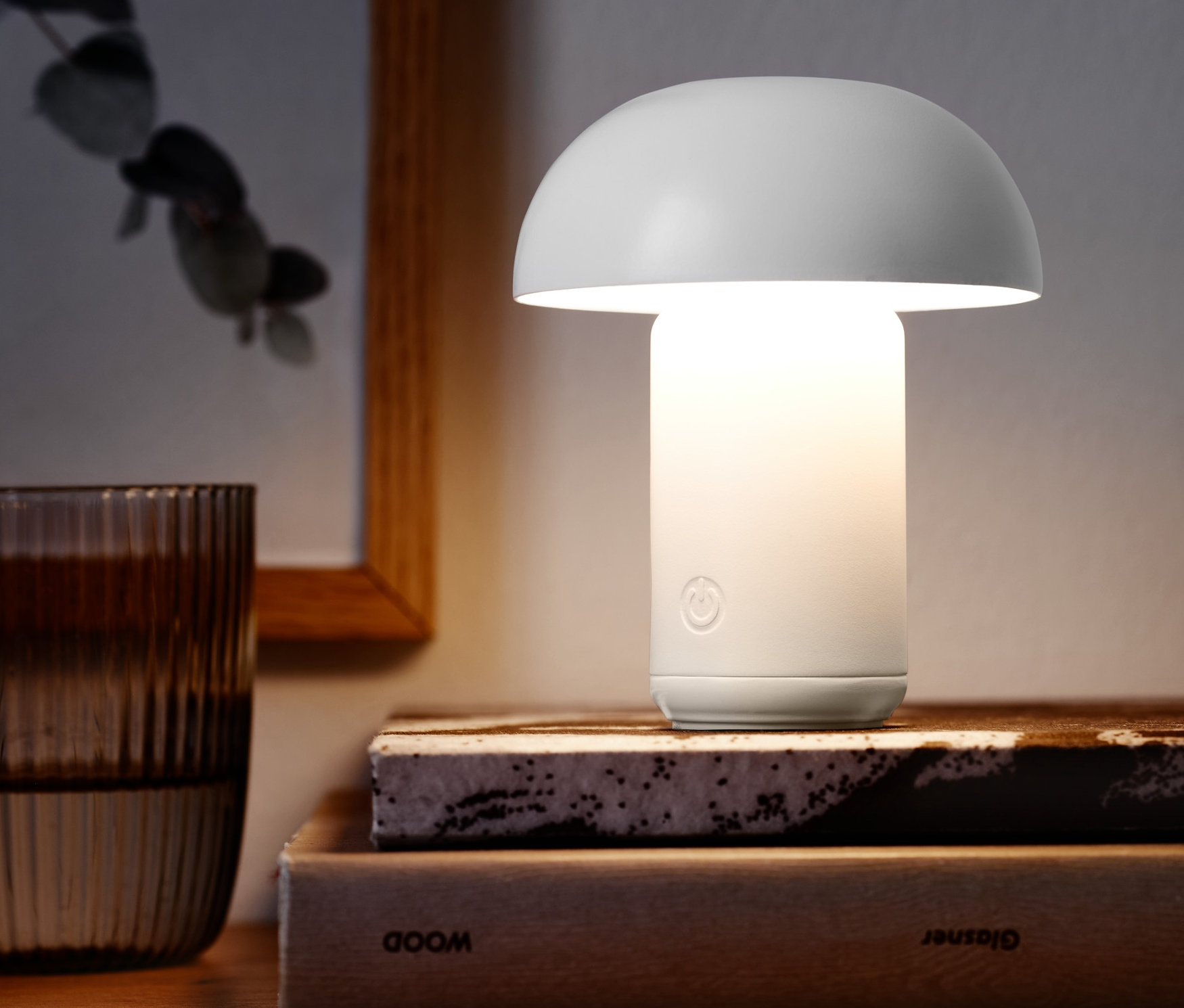 Akumulátorová stolní LED lampa stojí na knihách vedle sklenice vody.