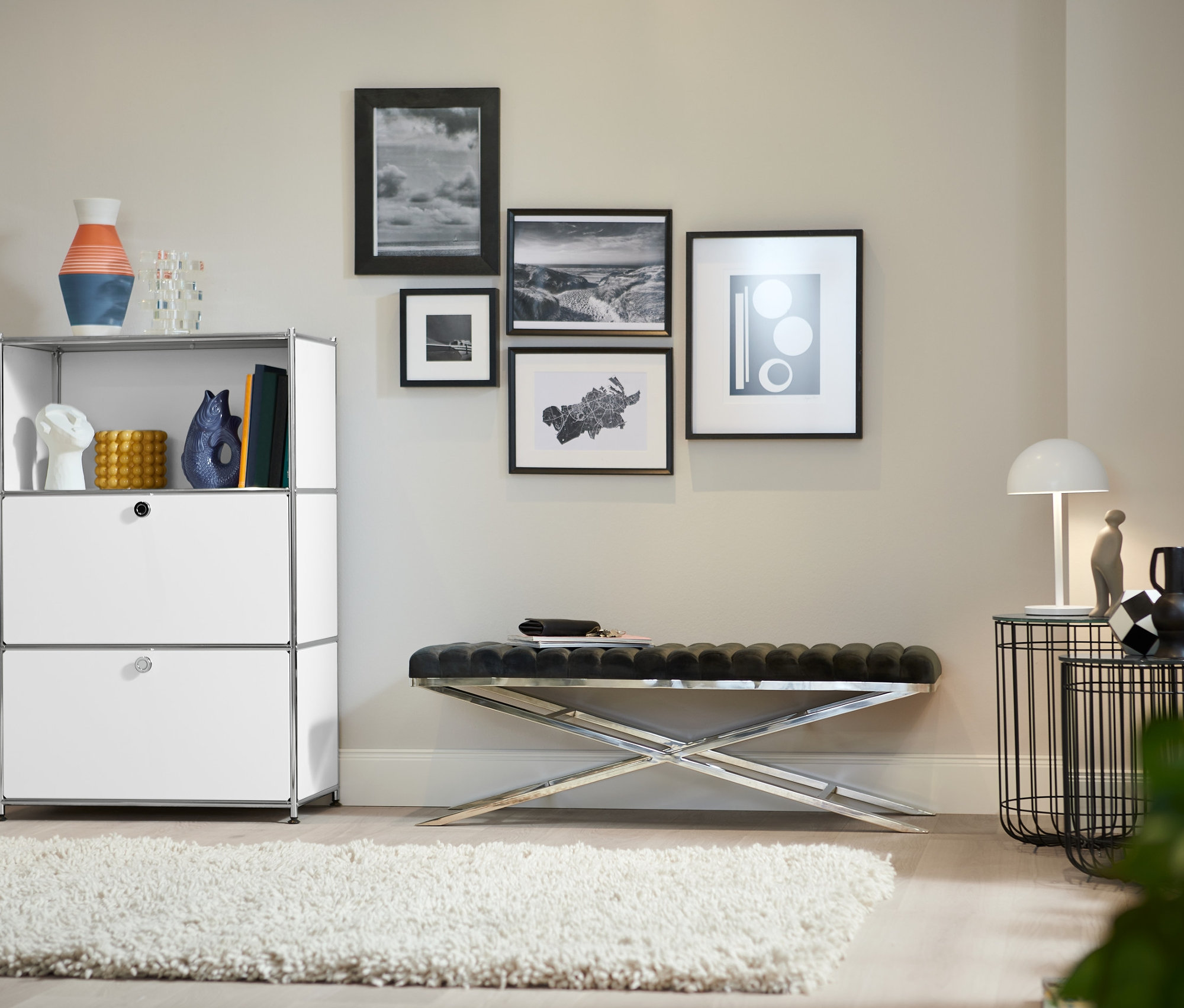 V obývacím pokoji stojí kovový regál s 2 bílými výklopnými dvířky, designová lavice s kovovou konstrukcí a designový barový vozík z kovu.