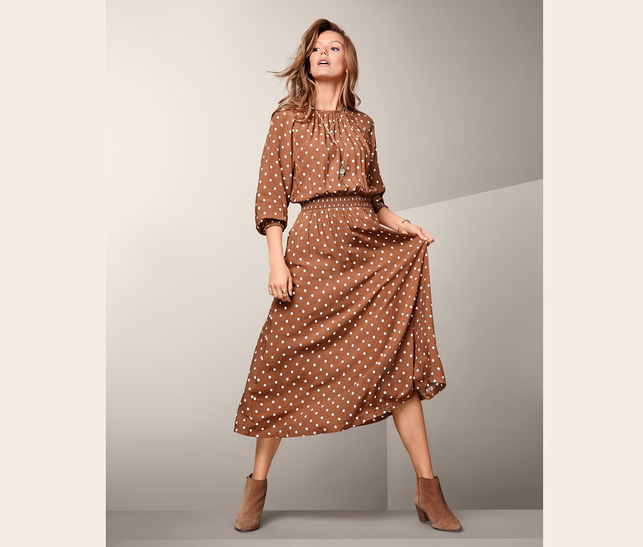 Žena pózuje v puntíkovaných midi šatech.