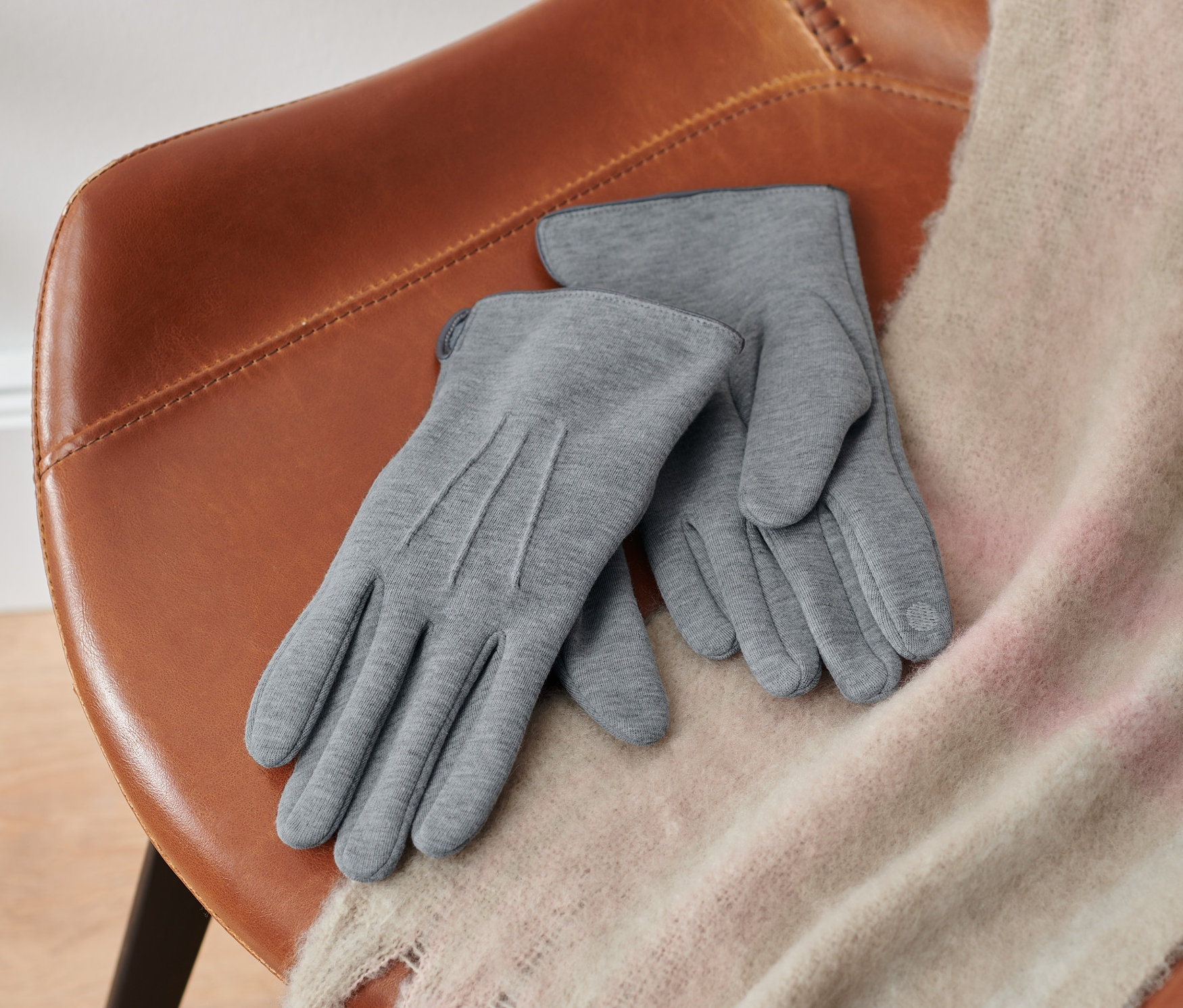 Na hnědé židli leží pár šedých melírovaných rukavic z teplákoviny.