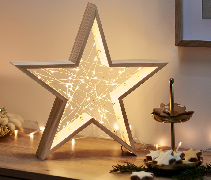 Na dřevěné komodě stojí dřevěná hvězda s LED světly, adventní věnec se svíčkou a etažér s cukrovím.